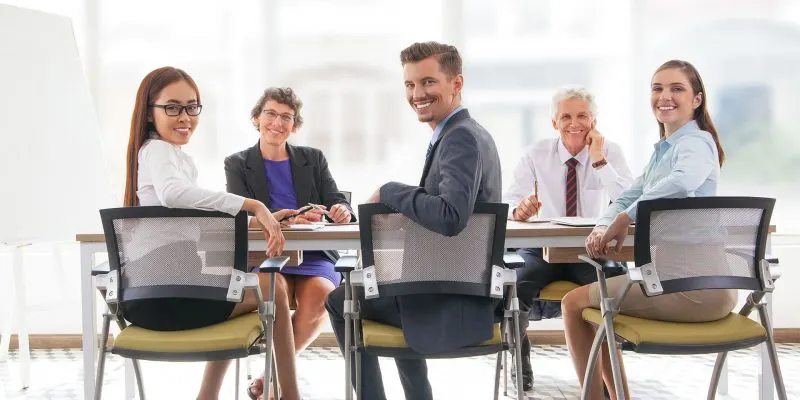 Business team having meeting in office Multi-ethnic smiling business team sitting at table and looking at camera. Business executives having meeting in office. Teamwork concept